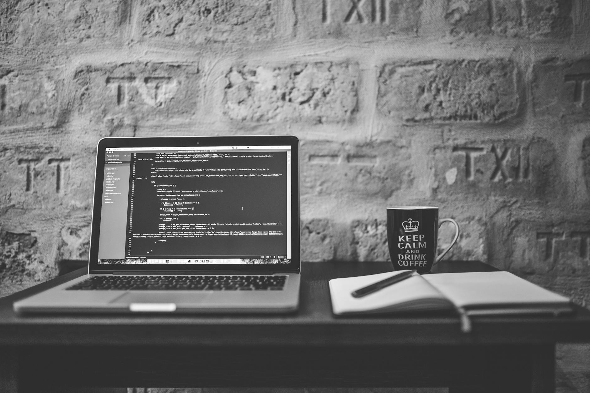 Czarno-białe biurko programisty z laptopem, kubkiem i notesem