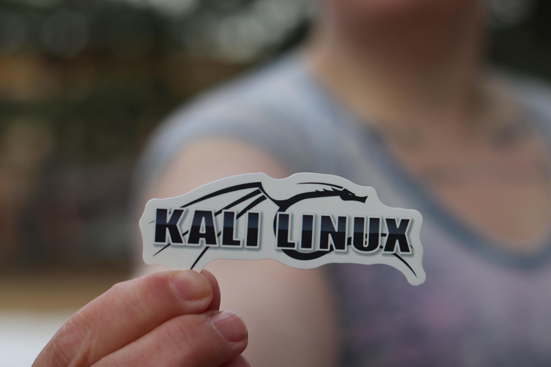 Dłoń trzymająca naklejkę Kali Linux, motyw cyberbezpieczeństwa
