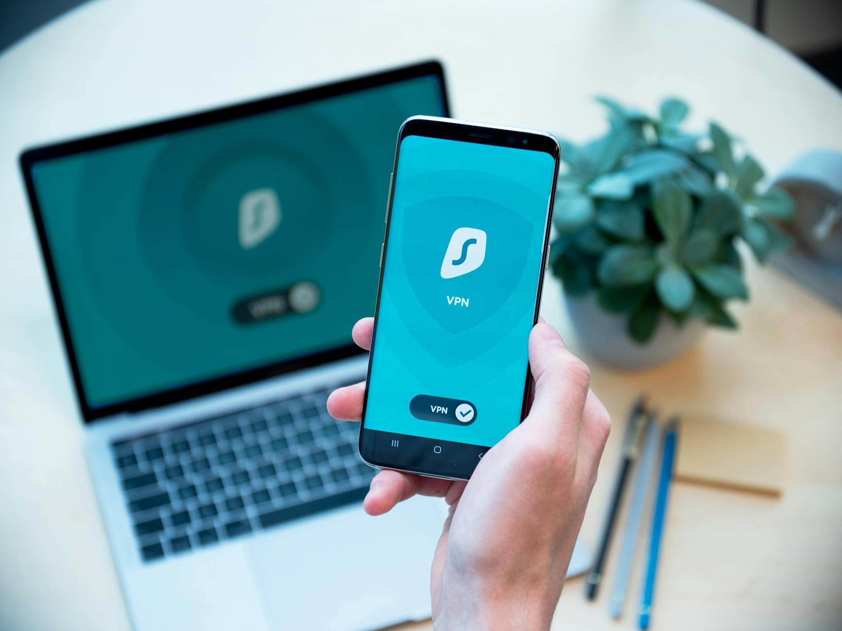 Dłoń trzymająca smartfon z aplikacją VPN, w tle laptop