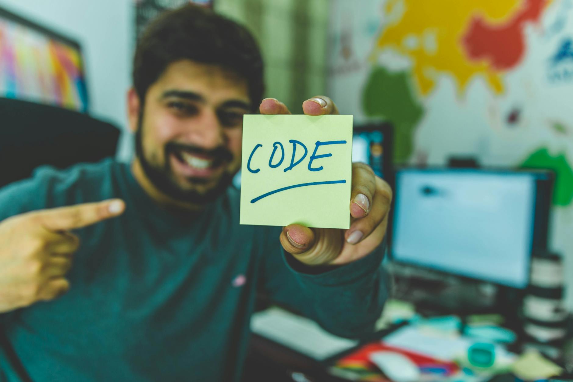 Programista w biurze uśmiecha się i wskazuje karteczkę z napisem code