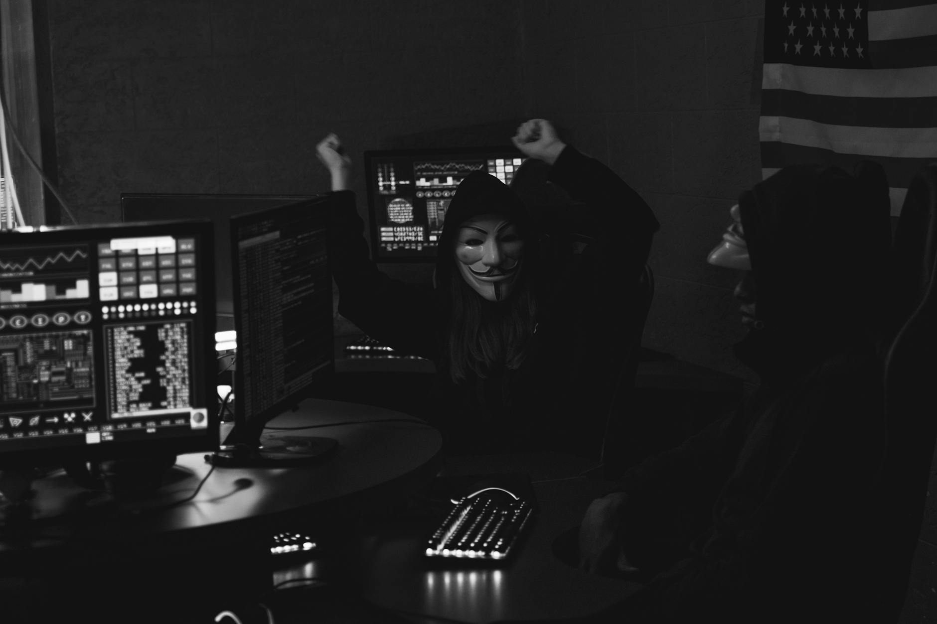 Grupa zamaskowanych hakerów świętuje udany atak w ciemnym pomieszczeniu