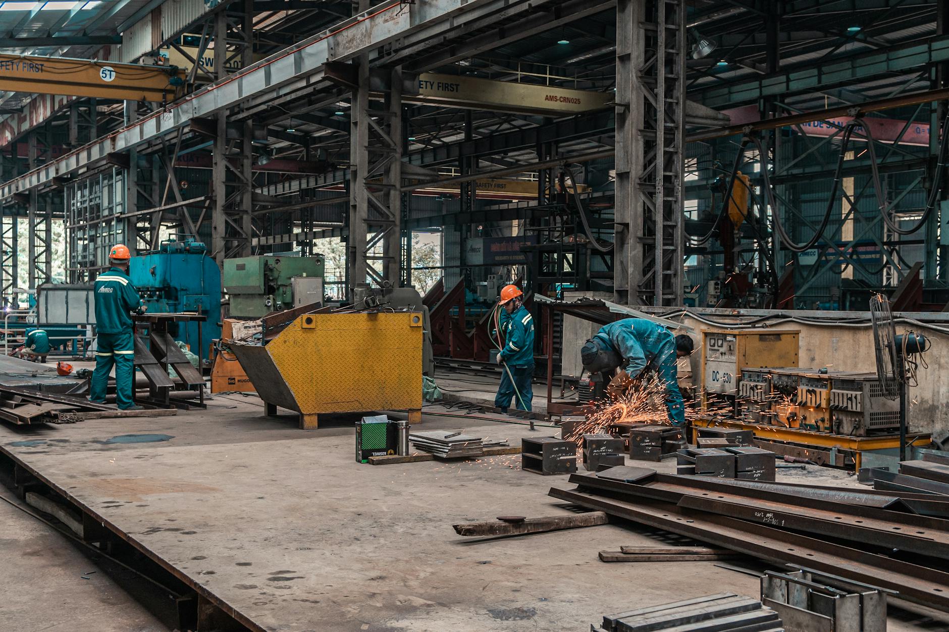 Pracownicy spawający metalowe elementy w hali produkcyjnej