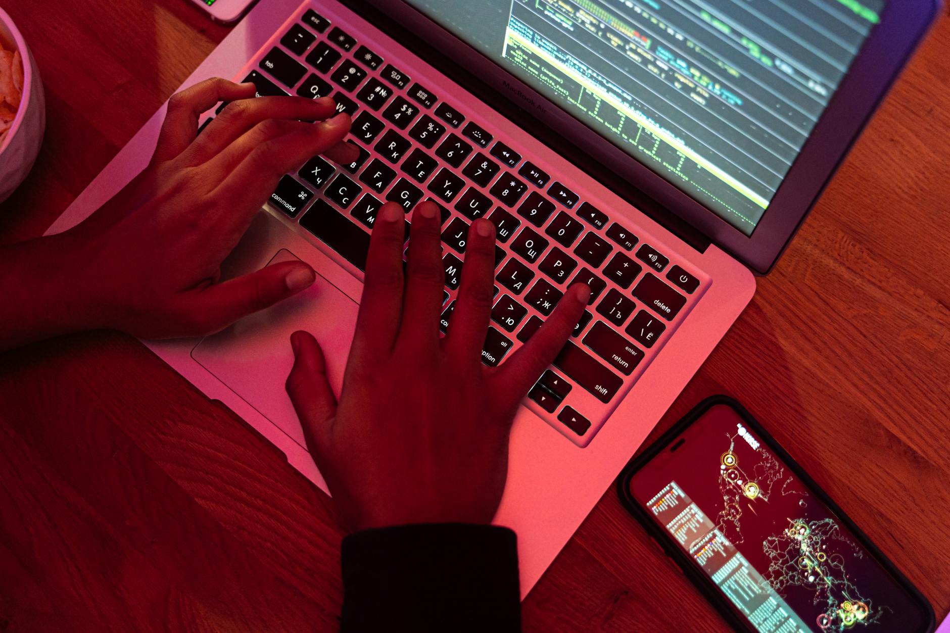 Programista pisze kod na laptopie nocą, obok leży smartfon